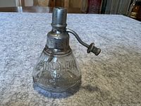 Clear glass bottle stamped with 'PINEOLEUM FOR MECHANICAL CONDITIONS' and topped with a metal spout and screw-on cap.
