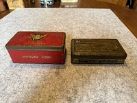 Top view of two vintage tobacco tins side by side on a fabric surface