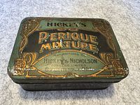 Top view of the rectangular metal tobacco tin with Hickey's Perique Mixture label, showing wear and rust spots.