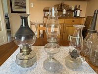 Three large oil lamps on table, showing overall size and design differences