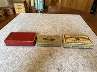 Top view of all three cigarette tins aligned side by side showing their size difference and designs.