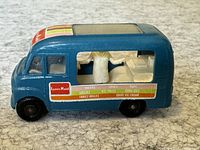 Front-left side view of blue ice cream truck showing driver's cab, side windows, interior with figure, and colorful decals.
