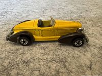 Side view of the yellow vintage Hot Wheels roadster car showing black fenders and detailed chrome parts.