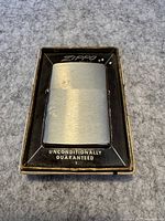 Close-up of vintage brushed metal Zippo lighter in original black interior box.