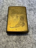 Front view showing gold coloured Zippo lighter with 'Winston' engraving and flying eagle design.