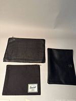 Top view of three black pouches on white background, one large leather, one Herschel fabric with label, one medium leather pouch