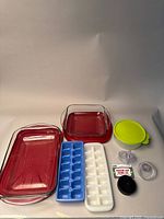 Two red Anchor Glass baking dishes with plastic lids, two ice cube trays (blue and white), a small green Tupperware container with lid, and three different regular mouth mason jar lids.