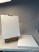Wooden art box with easel holding a blank canvas, three additional blank canvases stacked beside it.
