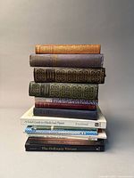 Photo of 11 books stacked vertically. Six books are vintage leather-bound with detailed gold spine embossing. Five books are modern paperbacks related to poetry, plays, and plants.