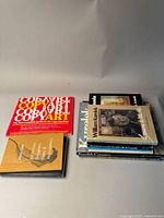 View of ten art and design books stacked on a white surface, including the bright red 'Copy Art' guide and two books related to William Kurelek.