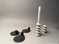 Photo of two neutral colour ceramic candle stick holders with stacked ridged design and three grey metal candle holders with ridged base arranged together on a white surface.