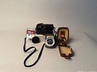 Photo showing the Canon A35 F camera, Gossen Lunasix light meter, lens cap, battery pack, and light meter case laid out on a flat surface.