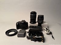 Top-down shot showing Canon Rebel XT body, two EF-S lenses, battery grip components, charger, lens hood ring and shutter cable