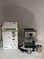 Front view of espresso maker with portafilter, tamper, frothing pitcher, and box.