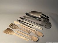 Overview of wooden spoons, metal tongs, skimmer, peeler, and spatula spread out on a countertop.