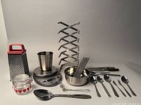 Photo showing kitchen scale, stainless steel bowl, metal skewers, metal expandable rack, grater, glass jar, and various cutlery items.