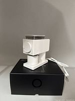 Fellow Ode Brew coffee grinder placed on its black original box, showing front with adjustment dial and attached power cord.