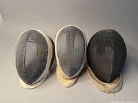 Front view of three used fencing masks showing metal mesh fronts and white padded rims and bibs.