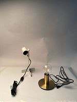 Two small IKEA lamps on a neutral background, one white adjustable spotlight lamp and one brass lamp with round base and exposed bulb, cords visible with switches.