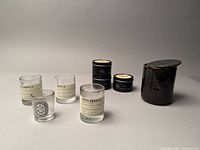 Collection of mini LeLabo, Dyptique, IKEA x Ben Gorham ceramic and Market Candle Company candle vessels shown from the side, illustrating variety in size and material.