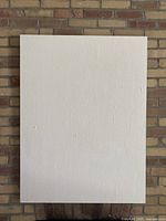 Front view of large white textured canvas wall art mounted on brick wall, showing subtle textured linear pattern on surface.