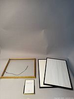 Set of four picture frames including two large black frames, one medium black frame, and one small gold frame with glass and hanging wire.