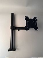 Photo of black metal monitor stand with vertical pole and articulating arm.