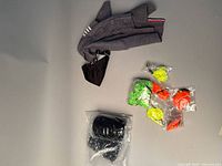 Gray knit cat sweater with bow tie accessory, assorted colorful ball toys, small black item wrapped in plastic.