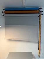 Backdrop stand holding three rolls of backdrop paper in blue, brown, and gray colors, displayed front view.