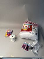 Lot items arranged on flat surface showing unopened colorful balloons, craft tie ribbon spool, polyester stuffing bag with owl design, two packs of metal cut tacks, and clear plastic clip.