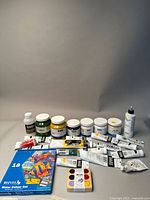Overview of the varied paint set displaying multiple tubes and jars of acrylic, oil, and watercolor paints in various colors. Reeves watercolor set and Beam paints box visible.