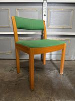 Front angle view of vintage mid-century modern chair with wooden frame and green fabric seat and backrest.