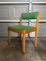 Front view of vintage mid-century modern chair showing wooden frame with green seat and backrest upholstery.