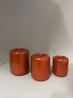 Three vintage orange cylindrical containers with closed lids, showing the set together.