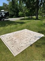 Full view of rectangular beige rug with brown floral patterns laid on grass outdoors.