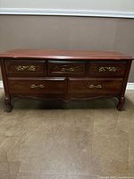 Front view of cherry wood chest showing top surface and 5 drawers with brass handles and carved legs.