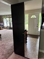Side view showing tall black cabinet closed with two doors, positioned near a doorway in a living space.