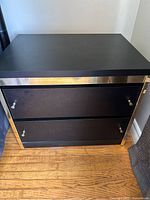 Front angle view of black wooden nightstand with 2 drawers and gold trim on reflective surfaces visible.