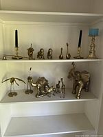 Image showing two shelves filled with polished brass animal figurines and candle holders, including elephants, giraffes, camels, cranes, lions, and buffalo.