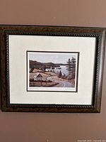 Framed art print showing rural landscape with houses near water, in carved brown wood frame with white matte, 13x16 inch