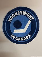 Full view of circular wall rug showing design of hockey puck, stick, and text 'Hockey Night in Canada' with blue and black color background.