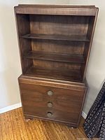 Front view of dark brown wooden cabinet showing 3 shelves on upper section and 3 closed drawers below.