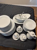 Top down photo showing stacks of plates, bowls, cups with saucers, pitcher, sauce boat with ladle and lids, arranged on black cloth.