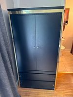 Front view of closed black wood cabinet with brass detailing along the top and edges, two doors, two drawers at the bottom.