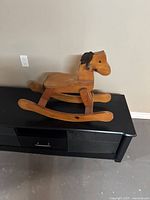 Side view of handmade wooden rocking horse showing natural wood color, carved head with black mane, and rocker base.