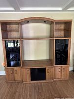 Front view of light oak composite entertainment center with open shelves, glass doors, and drawers.