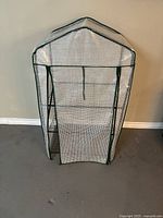 Front view of mini greenhouse with closed clear PVC cover and green metal frame, zipped front flap visible.