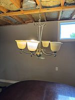 Six-light chandelier with frosted glass shades illuminated, hanging from ceiling with exposed wooden beams and ductwork.