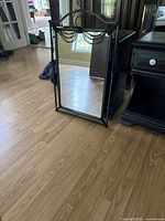 Full view of the wall mirror standing on floor showing rectangular shape, black metal frame, and arch with decorative chain detail at top.