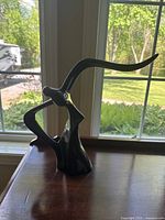 Front view of the dark brown ceramic modern sculpture placed on a wooden surface in front of a window with greenery outside.